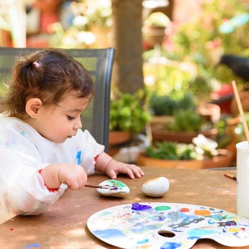 benefits of painting in early childhood - toddler painting on stones outdoors
