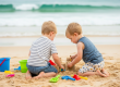 Two toddlers collaboratively building a sandcastle at a Sunshine Coast beach, demonstrating social skill development through natural play