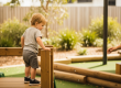 A toddler pauses at the top of a low timber climbing structure during safe risky play at a Sunshine Coast early learning centre.