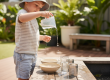 A preschool child explores volume and water flow through play at an outdoor water table at an early learning centre on the Sunshine Coast.